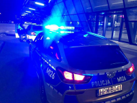 Radiowóz policyjny w porze nocnej z włączonymi sygnałami świetlnymi, w tle policjant Wydziału Ruchu Drogowego