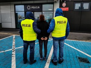 Policjanci z wydziału kryminalnego Komisariatu Policji III w Białymstoku ubrani w żółte kamizelki z napisem na plecach: &quot; policja&quot;. Policjanci trzymają za ręce zatrzymaną kobietę, która ma założone kajdanki na ręce  trzymane z tyłu