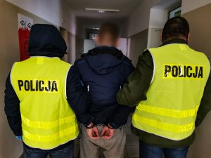 Policjanci z wydziału kryminalnego Komisariatu Policji III w Białymstoku ubrani w żółte kamizelki z napisem na plecach: &quot; policja&quot;. Policjanci trzymają za ręce zatrzymanego, który ma założone kajdanki na ręce  trzymane z tyłu