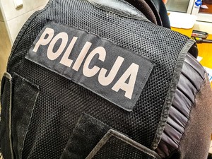 Policjant stojący tyłem w kamizelce z napisem policja